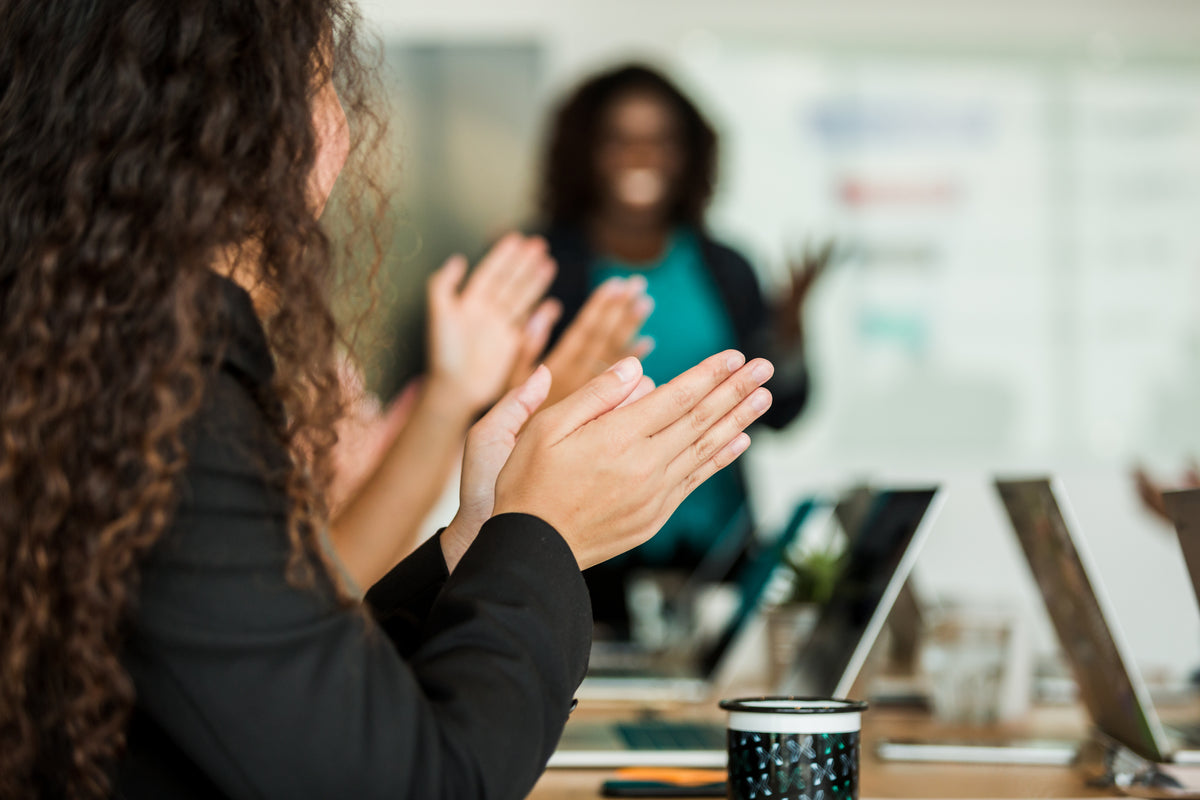 Meeting attendees clapping at a laptop-equipped conference table presentation
