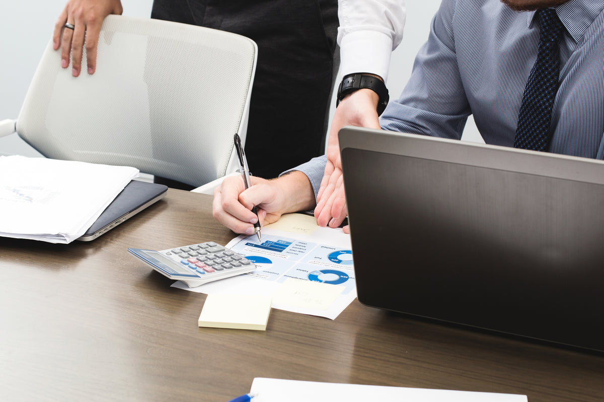 Business meeting at desk with laptop, calculator, and chart-filled documents