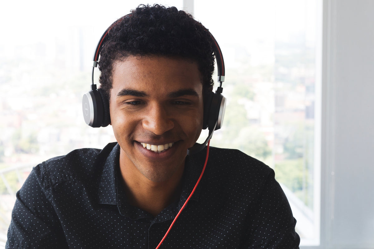 Smiling man wearing a headset, working at a desk by a window