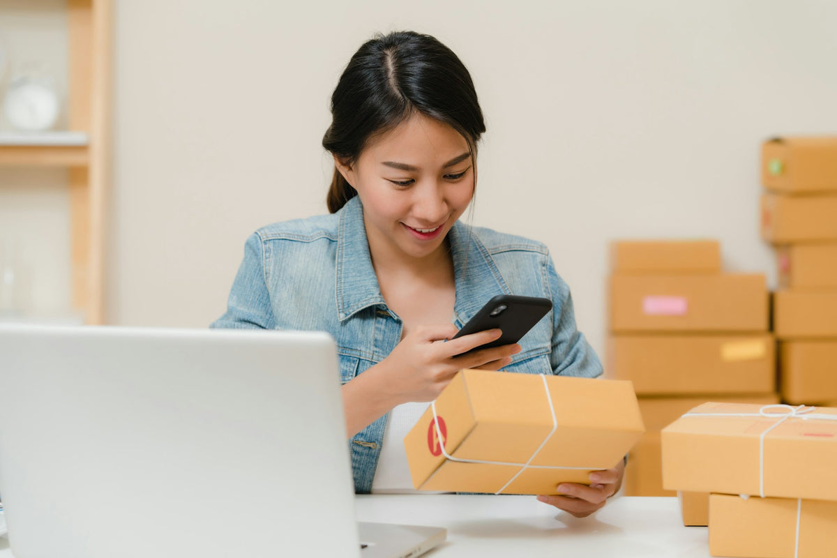 Small business owner checking online orders next to packed boxes