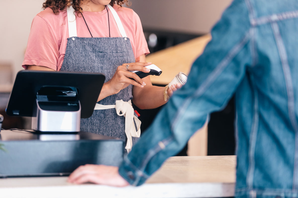 Apron-clad cashier scanning a customer's item at a store checkout counter