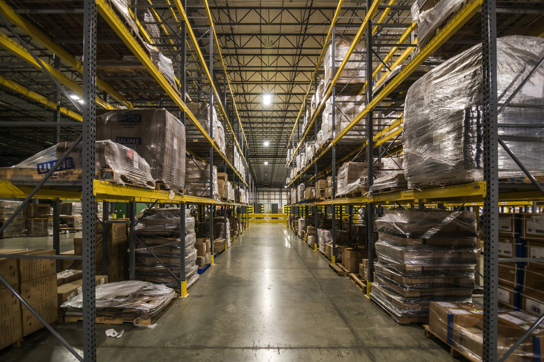 Warehouse aisle lined with tall pallet racks holding shrink-wrapped stacked goods